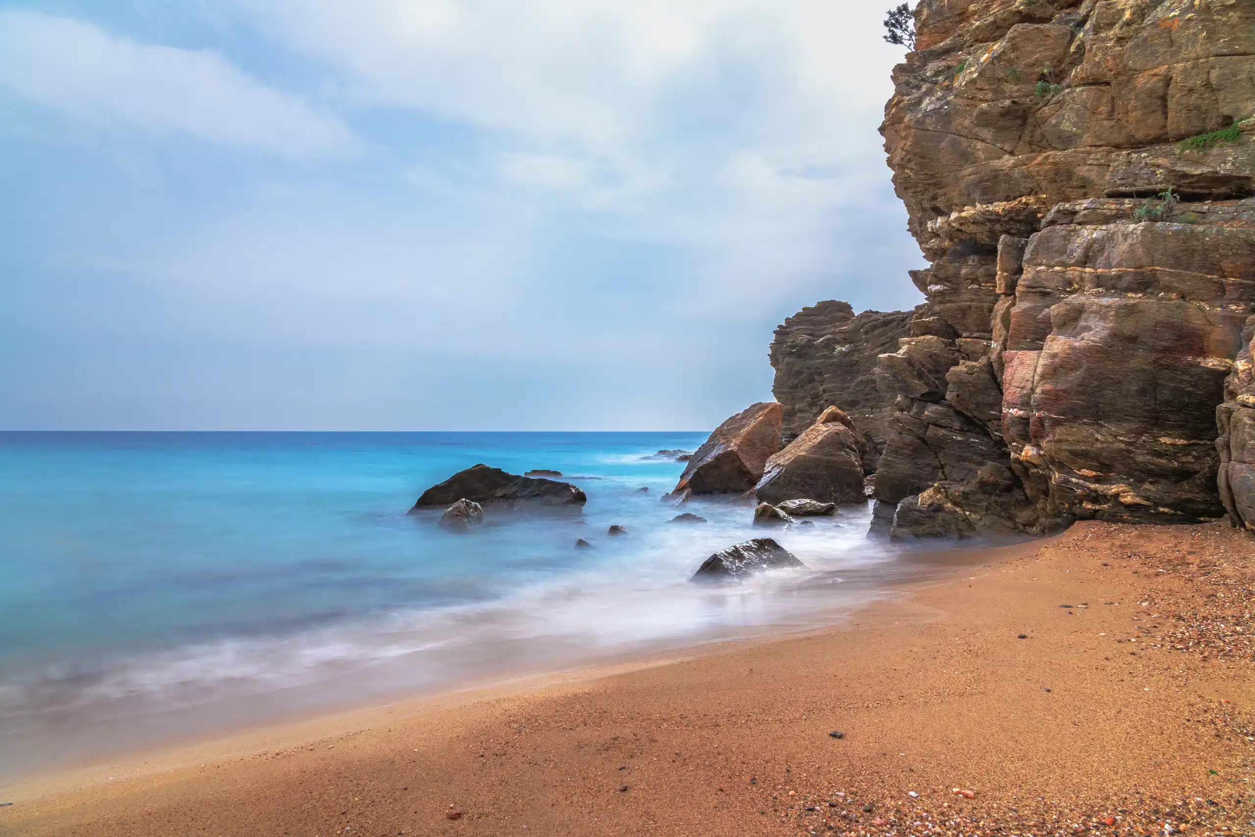 Plage dorée avec falaises rocheuses et mer turquoise