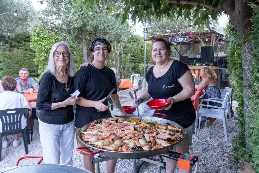 Trois femmes servant une grande paella en extérieur