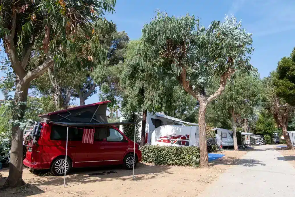 Van rouge aménagé dans un camping arboré